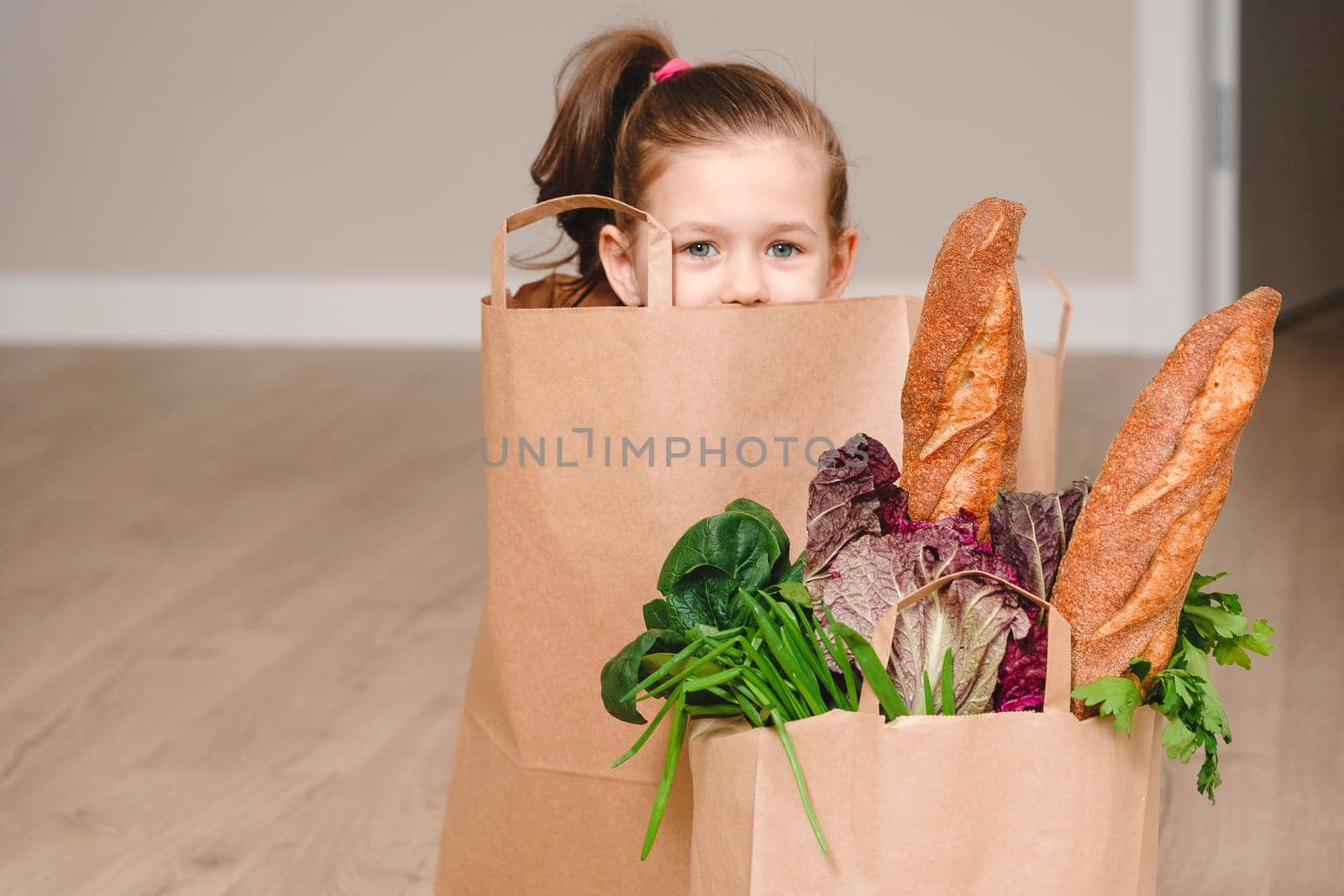 Little girl sitting in Paper bag hiding with vegetables and bread, grocery with copy space by Mariakray