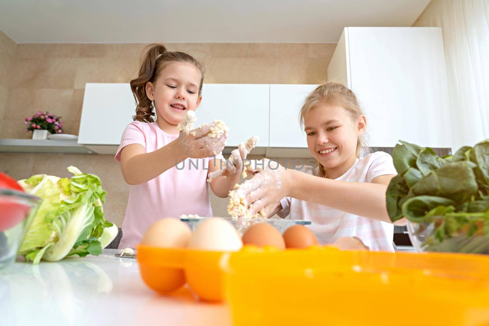 happy family funny kids are preparing the dough, bake cookies in the kitchen. sisters having fun together laughing by Mariakray