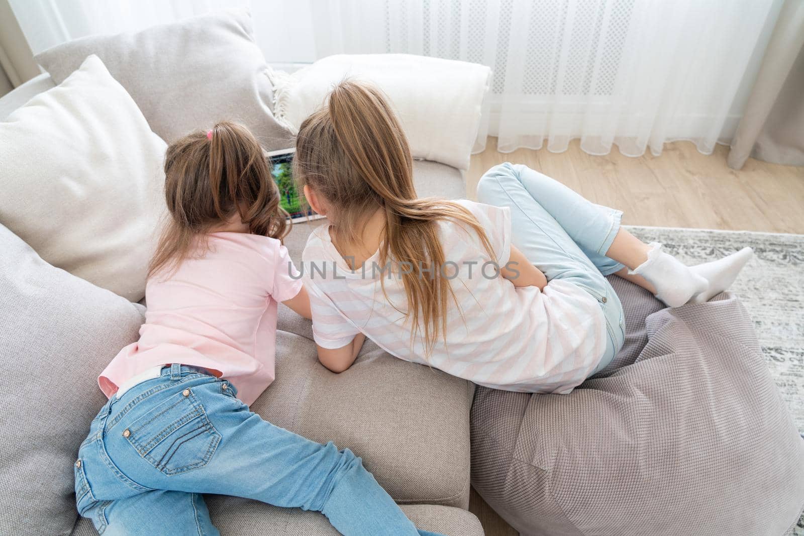 Two little sisters Lying On Couch And Using Tablet