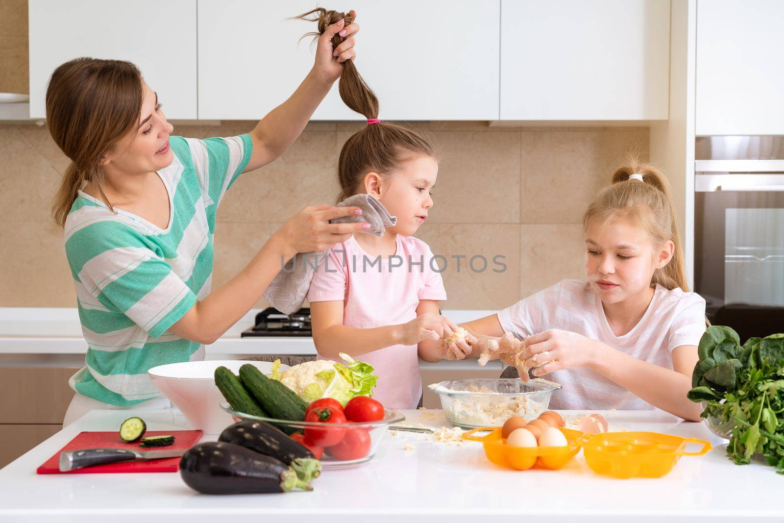 Mother and two daughters cooking in the kitchen and having fun, happy family and single mother concept by Mariakray