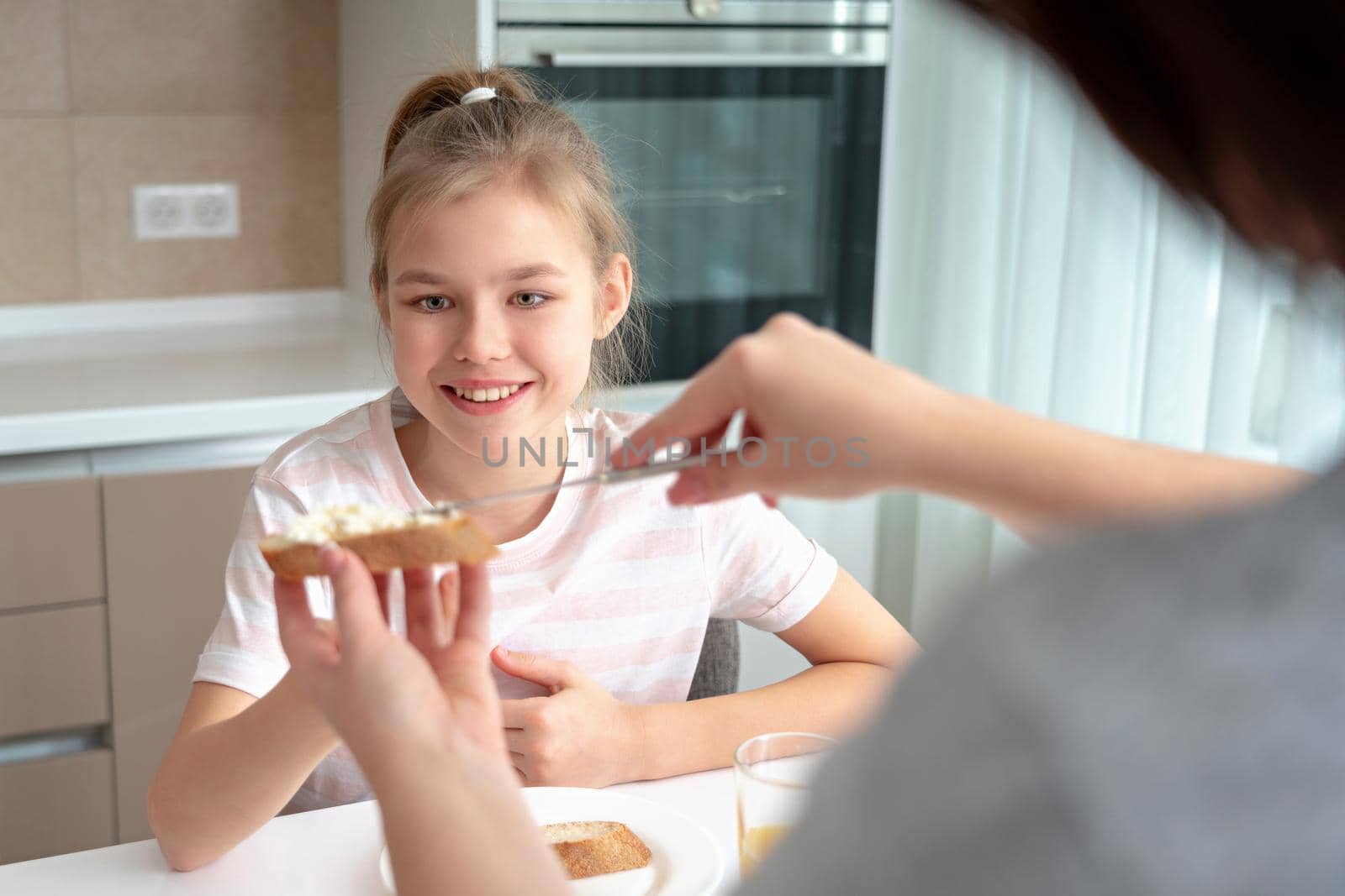 Young woman feeding her daughter with appetizing homemade sandwich for breakfast