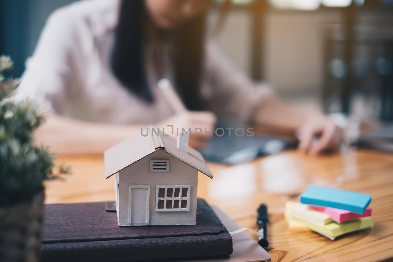 Architect woman using a digital tablet application to hand-draw a design house with a model on a wooden desk. Property idea in real estate.