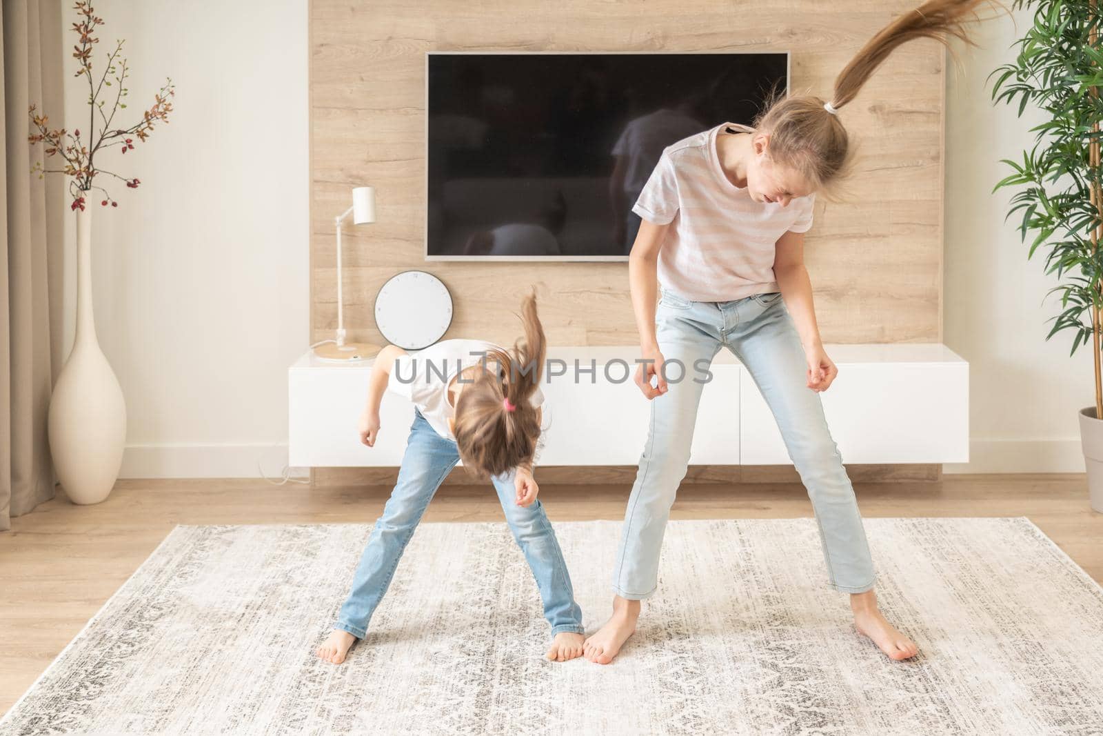 Two sisters having fun dancing in living room, happy family concept by Mariakray
