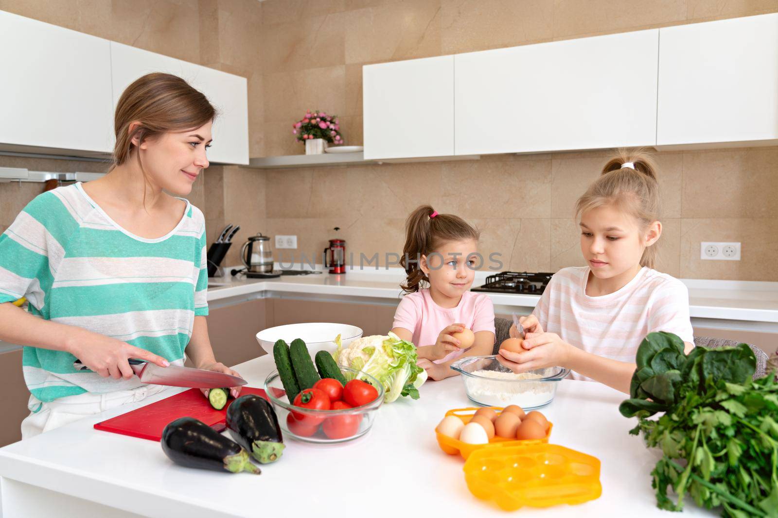 Mother and two daughters cooking in the kitchen and having fun, happy family and single mother concept by Mariakray