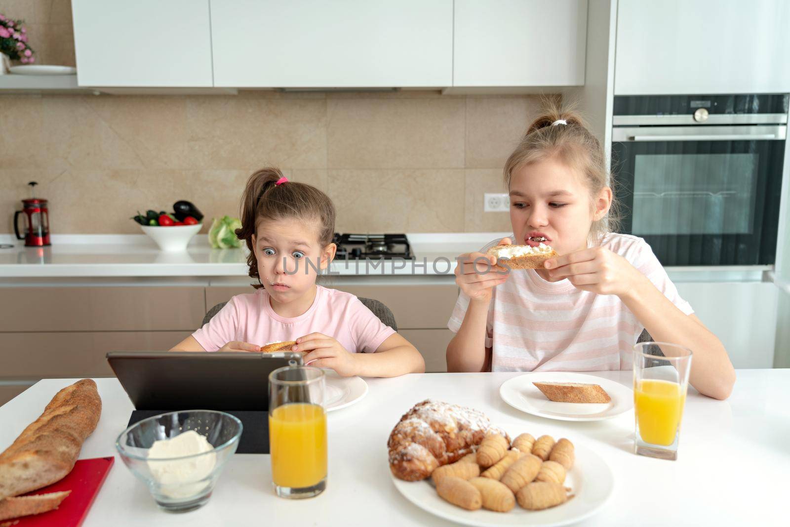 Two sisters having breakfast and watching cartoons on tablet together, happy family concept by Mariakray