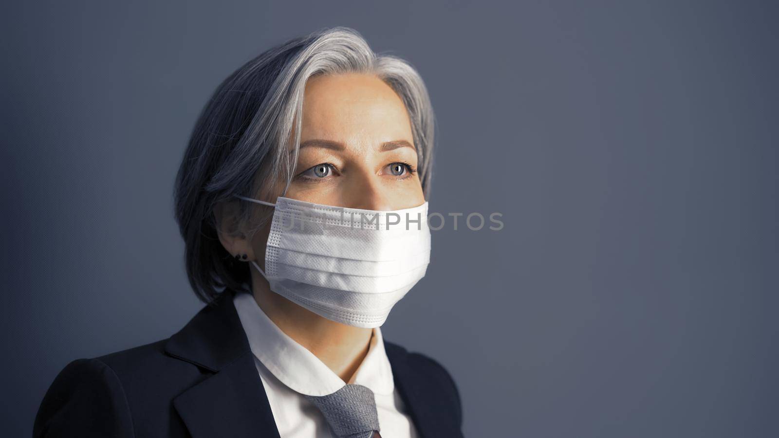 Gray haired businesswoman in protective mask looking at side, Masked fashion Caucasian woman in formal wear isolated on gray background. Epidemic concept.