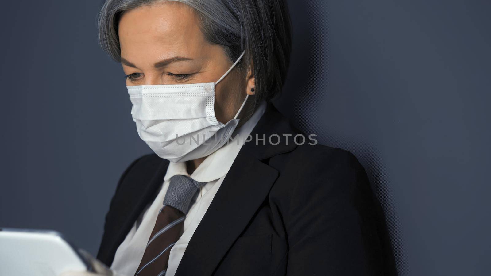 Mature masked business woman using digital tablet. Close up shot by LipikStockMedia