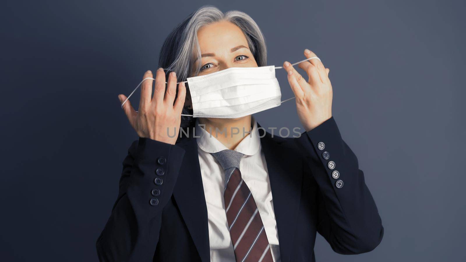 Mature business woman holding protective mask before her face. Quarantine concept.