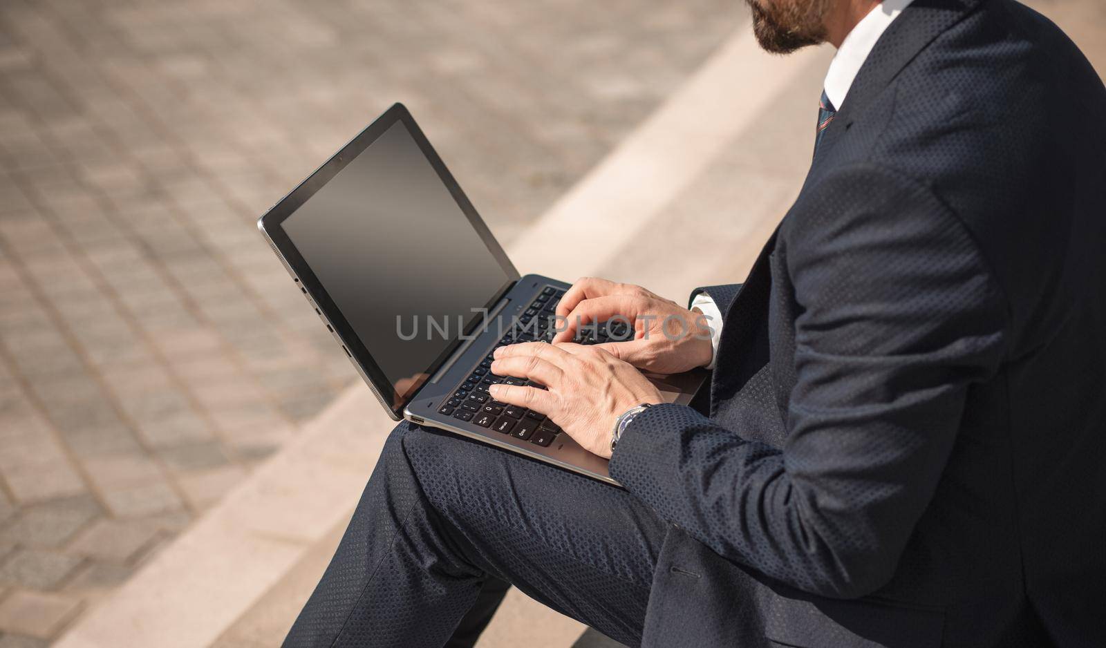 Adult man in business suit sits with laptop on the street. Side view of Caucasian man working on the steps. High quality photo by LipikStockMedia