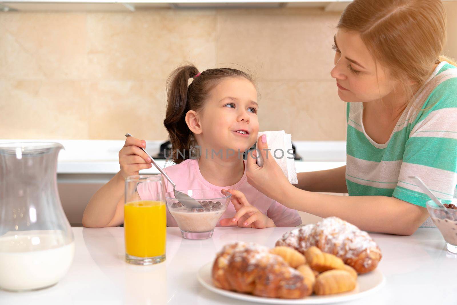 Mother having breakfast with her daughter at a table in kitchen, happy single mother concept by Mariakray
