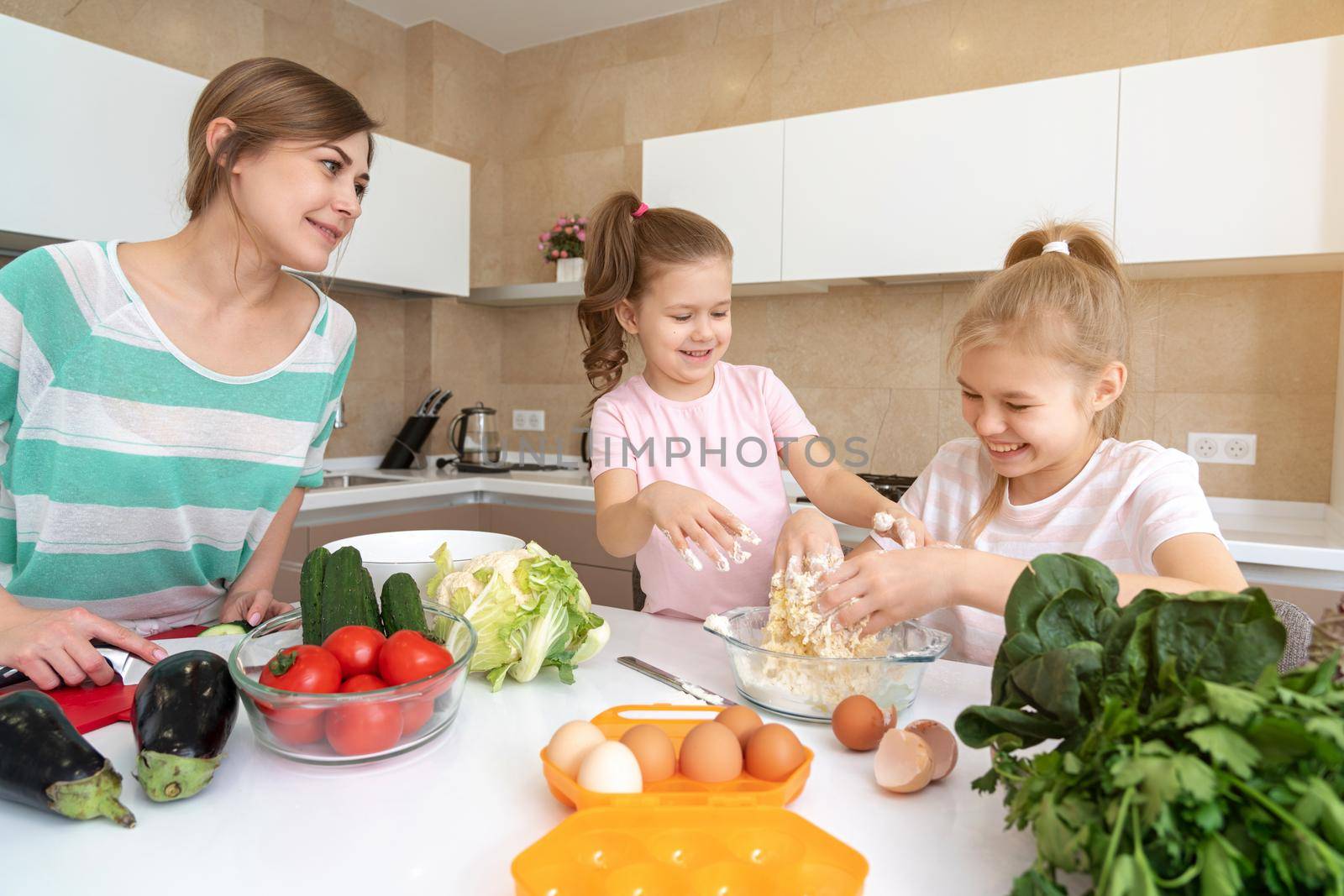 Mother and two daughters cooking in the kitchen and having fun, happy family and single mother concept by Mariakray
