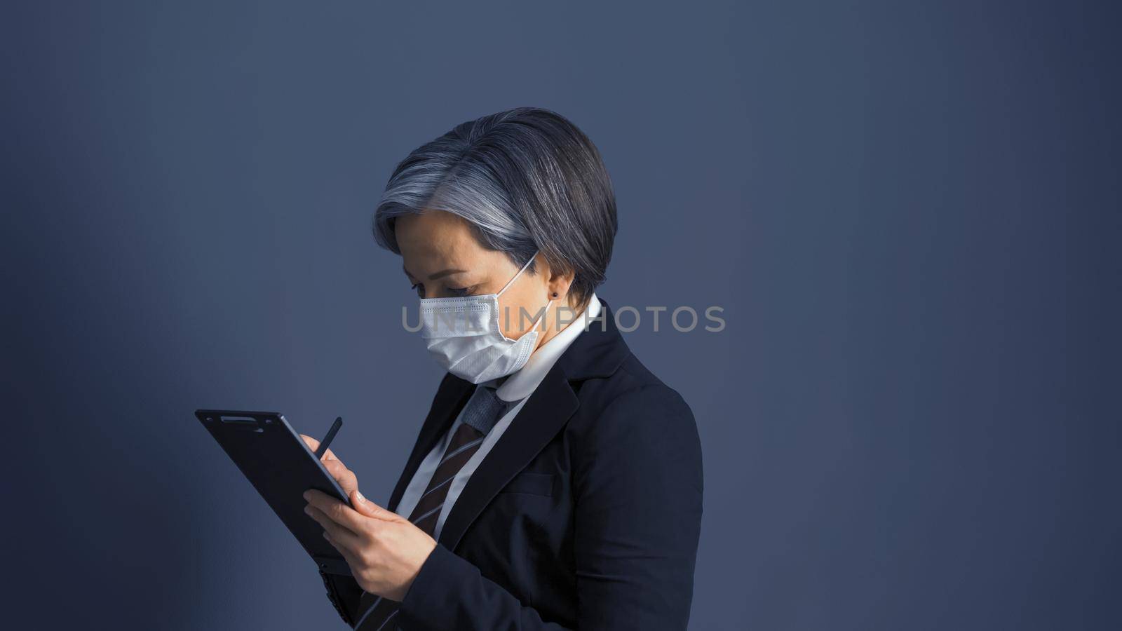 Aged Caucasian businesswoman wearing face mask and black suit writing on blank. Working in a pandemic concept. Side view.