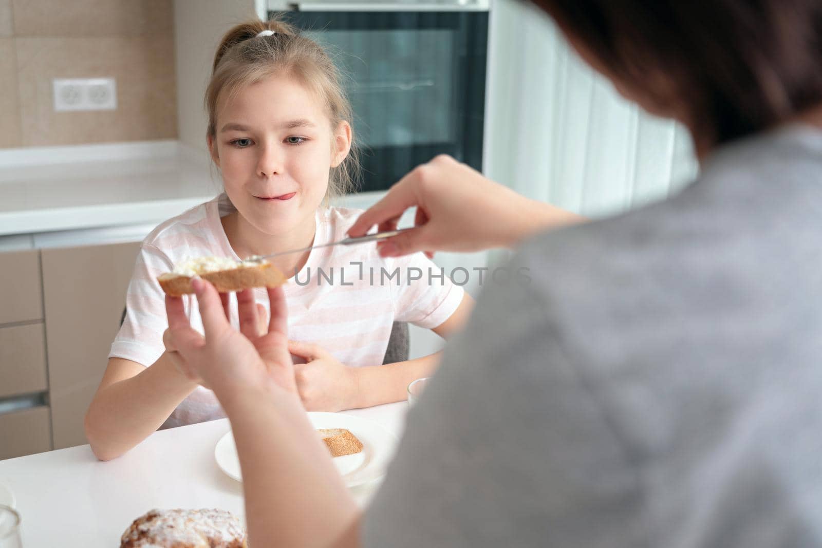 Young woman feeding her daughter with appetizing homemade sandwich for breakfast