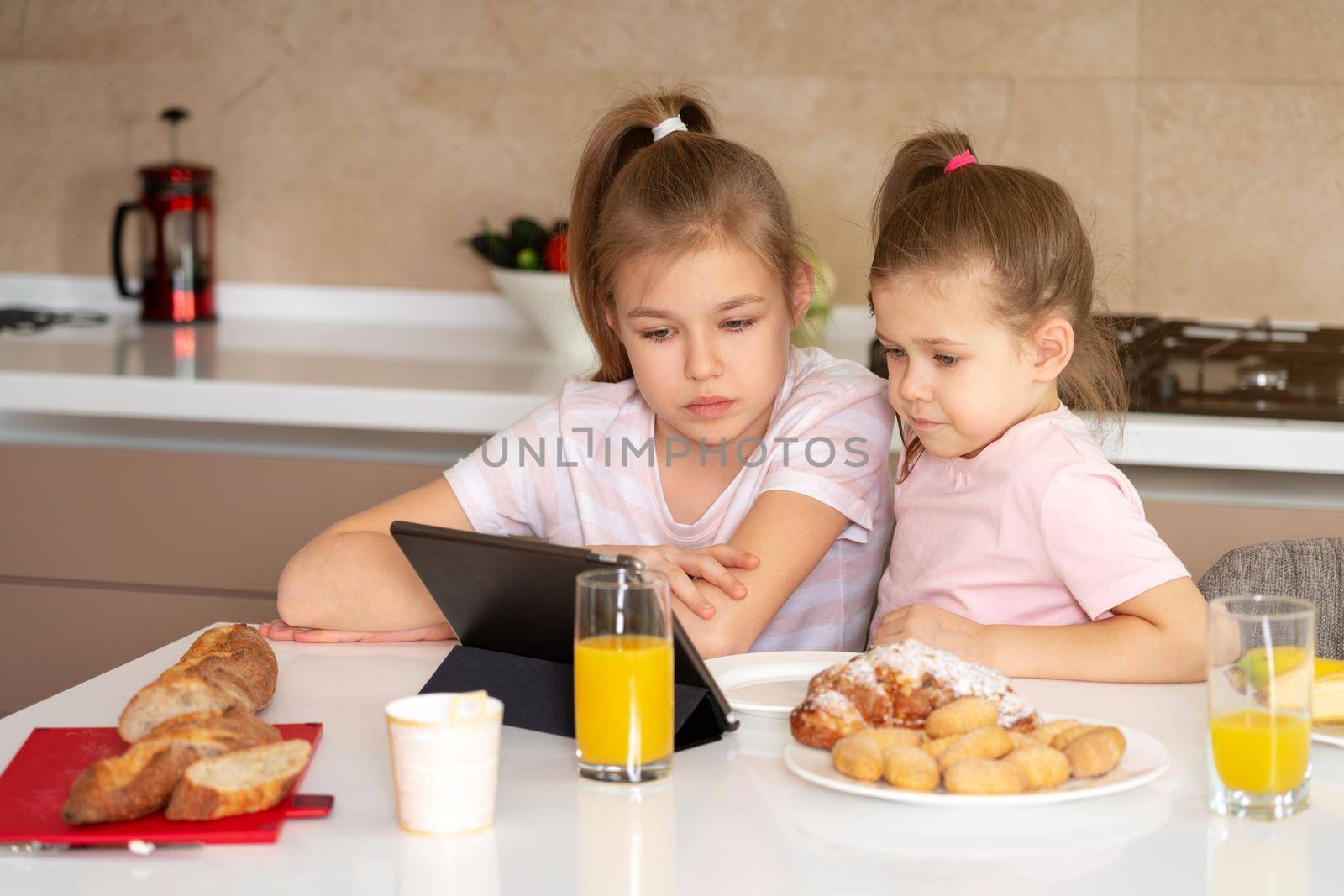 Two sisters having breakfast and watching cartoons on tablet together, happy family concept by Mariakray