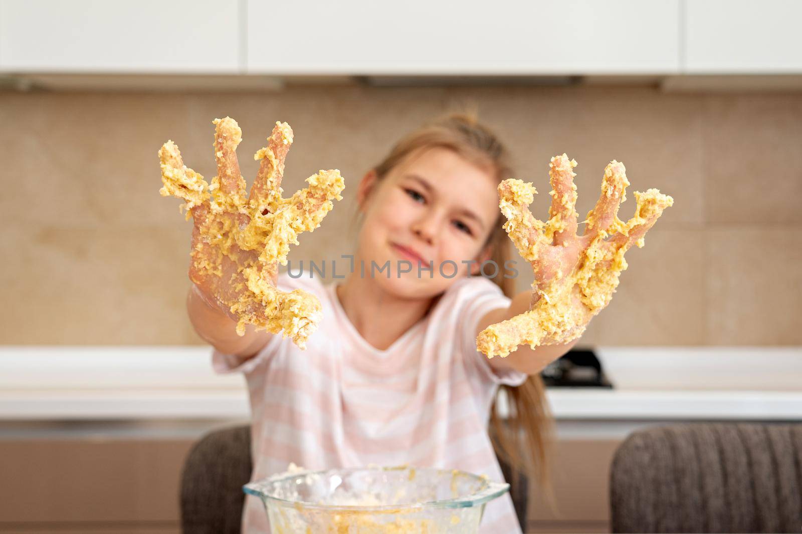 Portrait of a little girl in the kitchen dressed as a professional cook playing with flour, gets her hands dirty and smiles happy. Concept of: nutrition, cooking school, education and game.