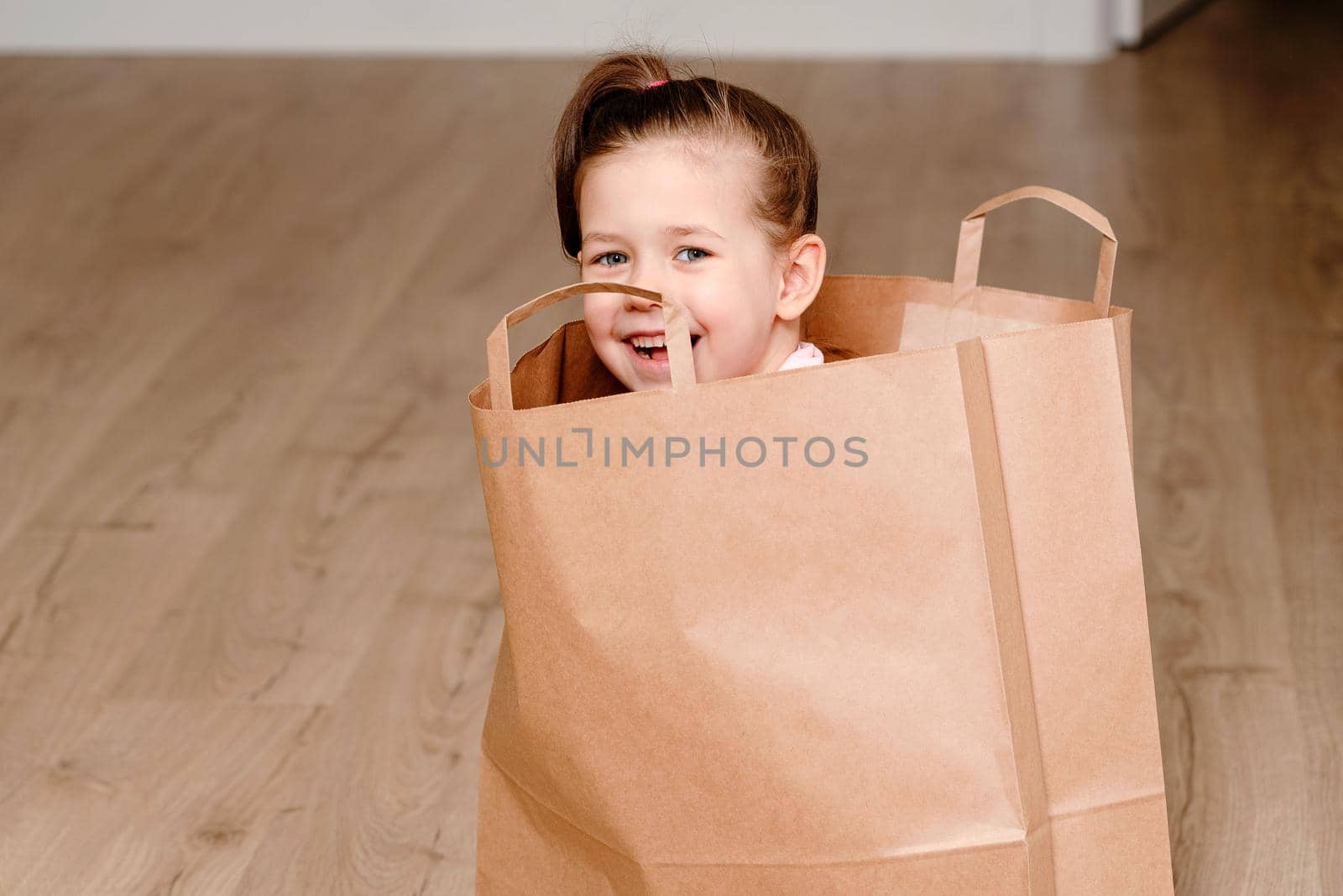 Little girl sitting in Brown paper shopping bag