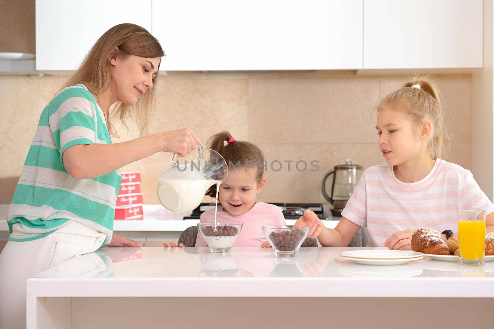 Mother serving breakfast to her two daughters at a table in kitchen, happy single mother concept by Mariakray