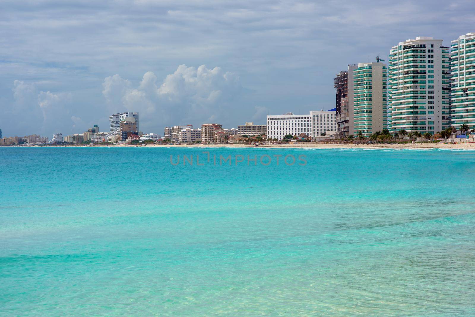 View of sandy beach panorama at bay of Caribbean Sea in mexican city, white hotels buildings and jet skis, clear water and blue sky in warm sunny winter day