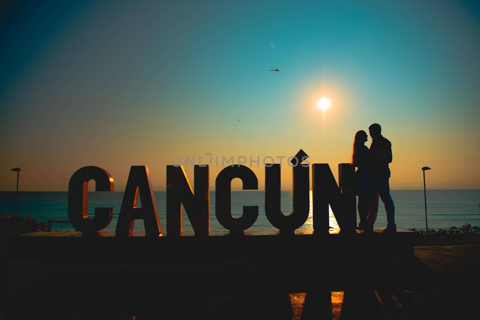 The silhouette of a man and a woman near the inscription Cancun in the background of the sea.