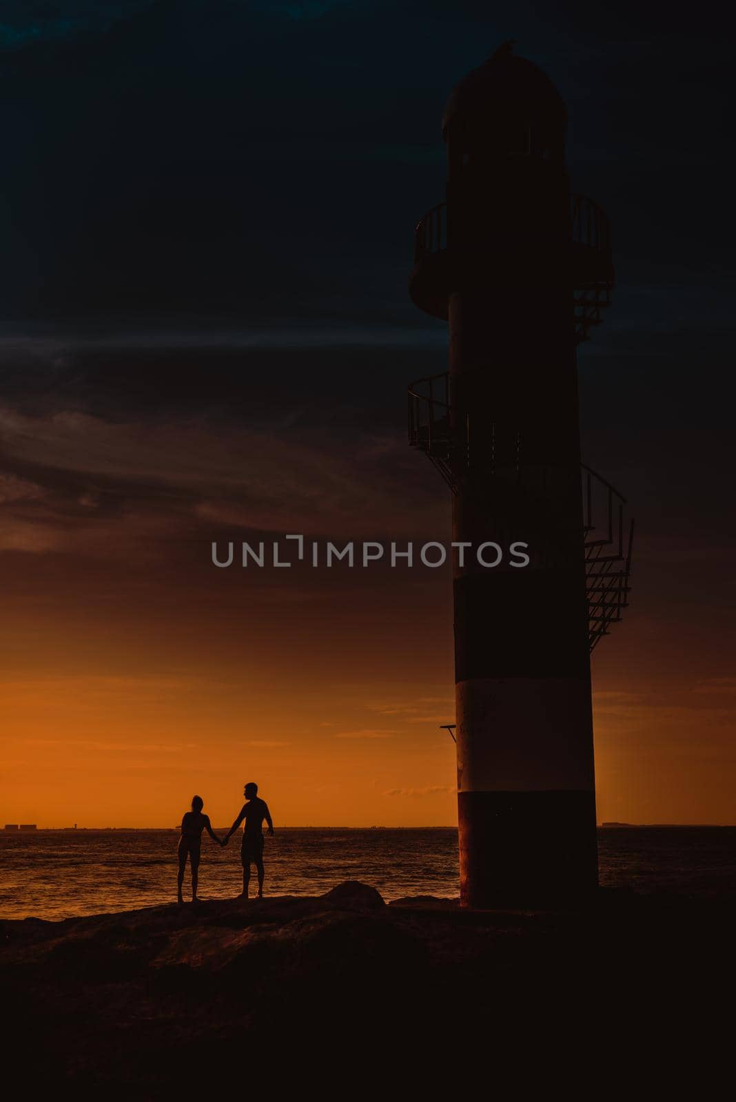 The silhouette of a couple and a huge lighthouse against the backdrop of the sea and the setting sun. Mexico.