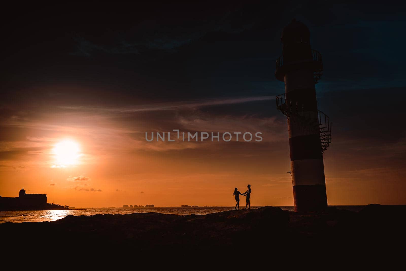 The silhouette of a couple and a huge lighthouse against the backdrop of the sea and the setting sun. Mexico.