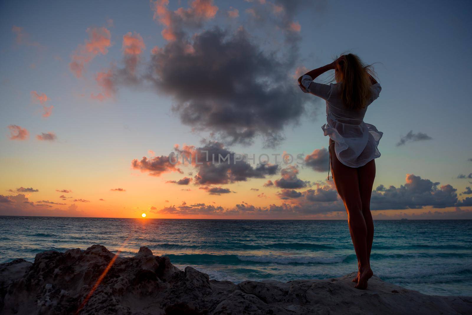 Slender blonde woman admires the sunrise at sea.