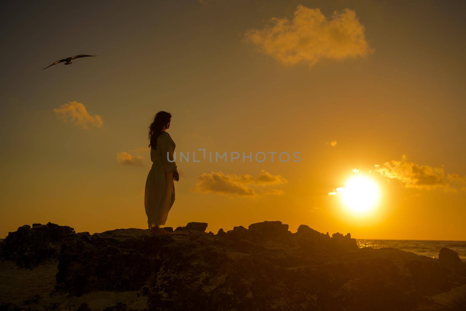 Slender blonde woman admires the sunrise at sea.