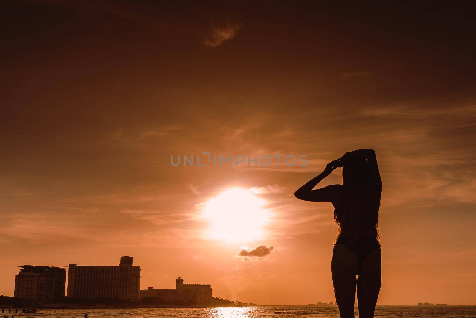 Slender blonde woman admires the sunrise at sea.