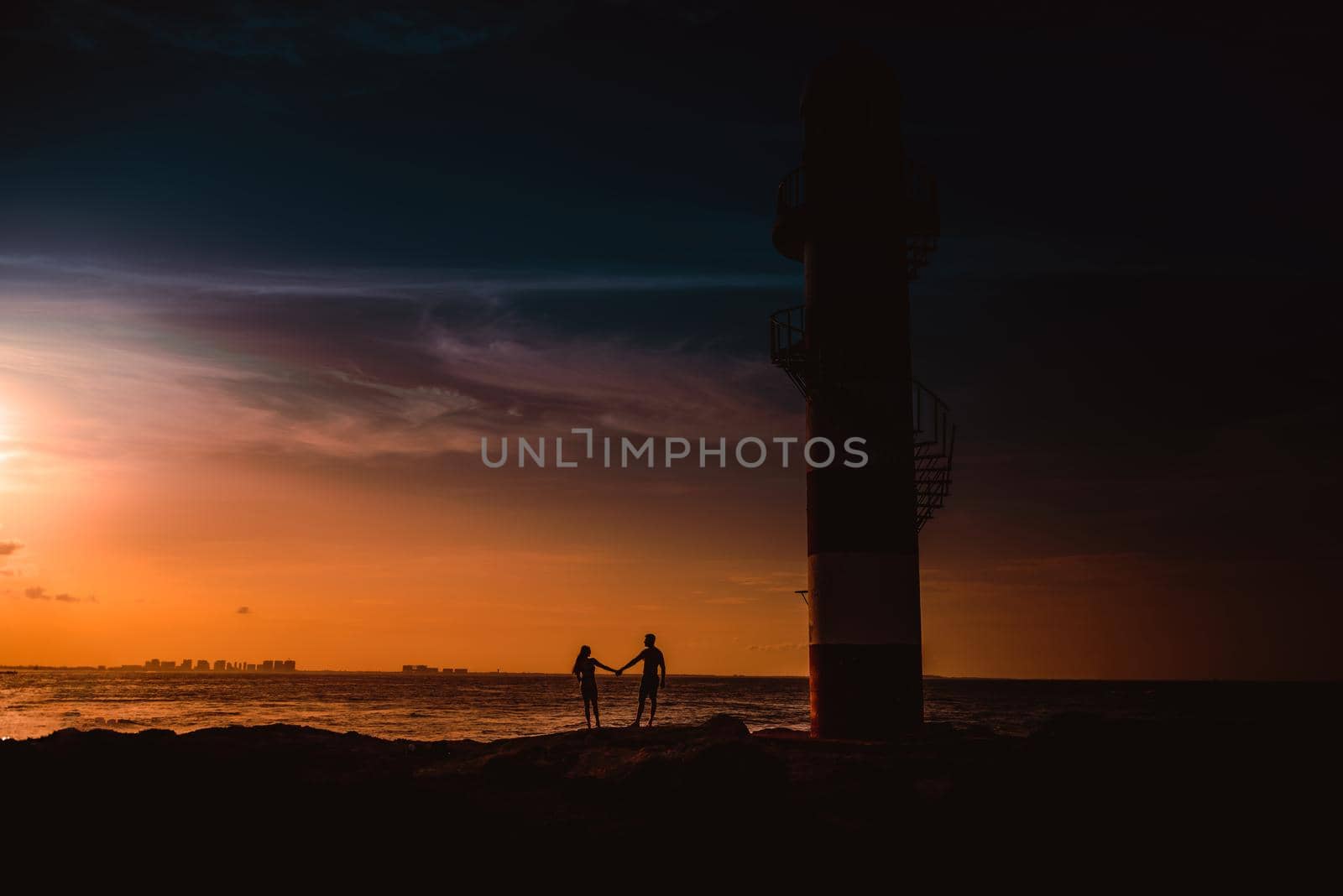 The silhouette of a couple and a huge lighthouse against the backdrop of the sea and the setting sun. Mexico.