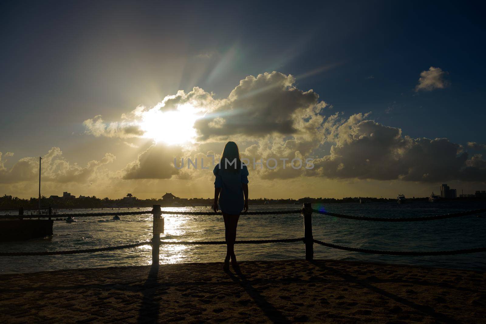 Slender blonde woman admires the sunrise at sea.