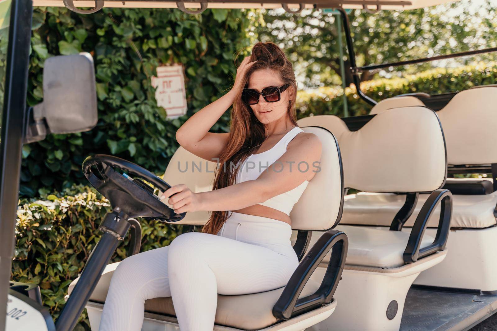 A middle-aged woman is driving a car for transporting tourists. Electric car, Tourist bus. Car for transporting people around the hotel, park, golf club.