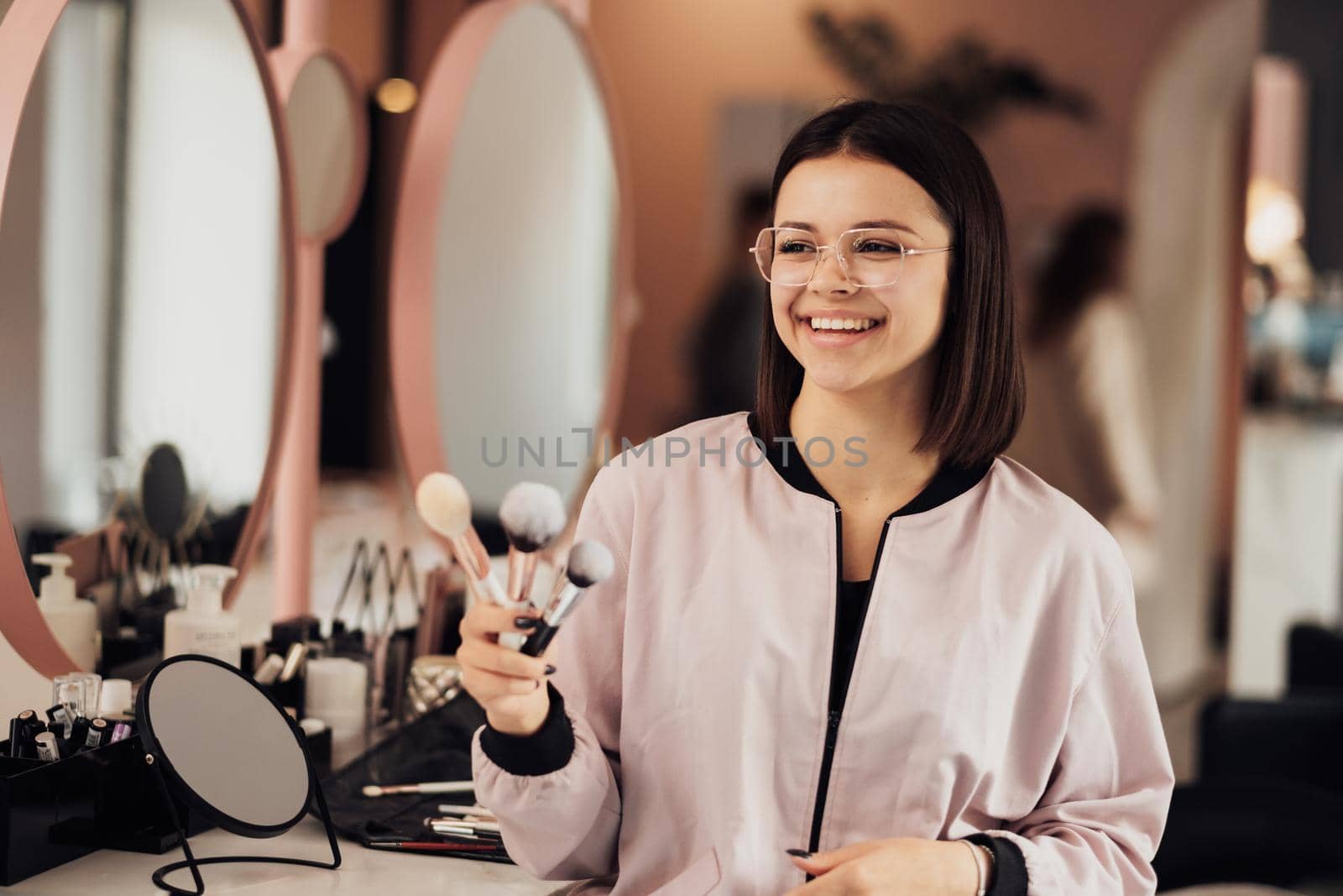 Portrait of Young Cheerful Female Make Up Artist Standing in Beauty Salon, Caucasian Woman in Glasses Holding Brushes at Workplace