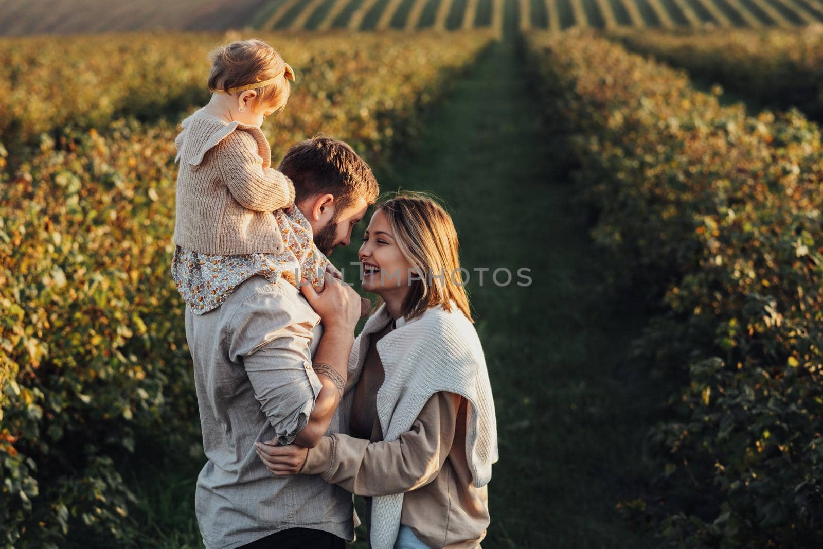 Happy Young Family Outdoors, Mother and Father with Their Baby Daughter at Sunset in Field