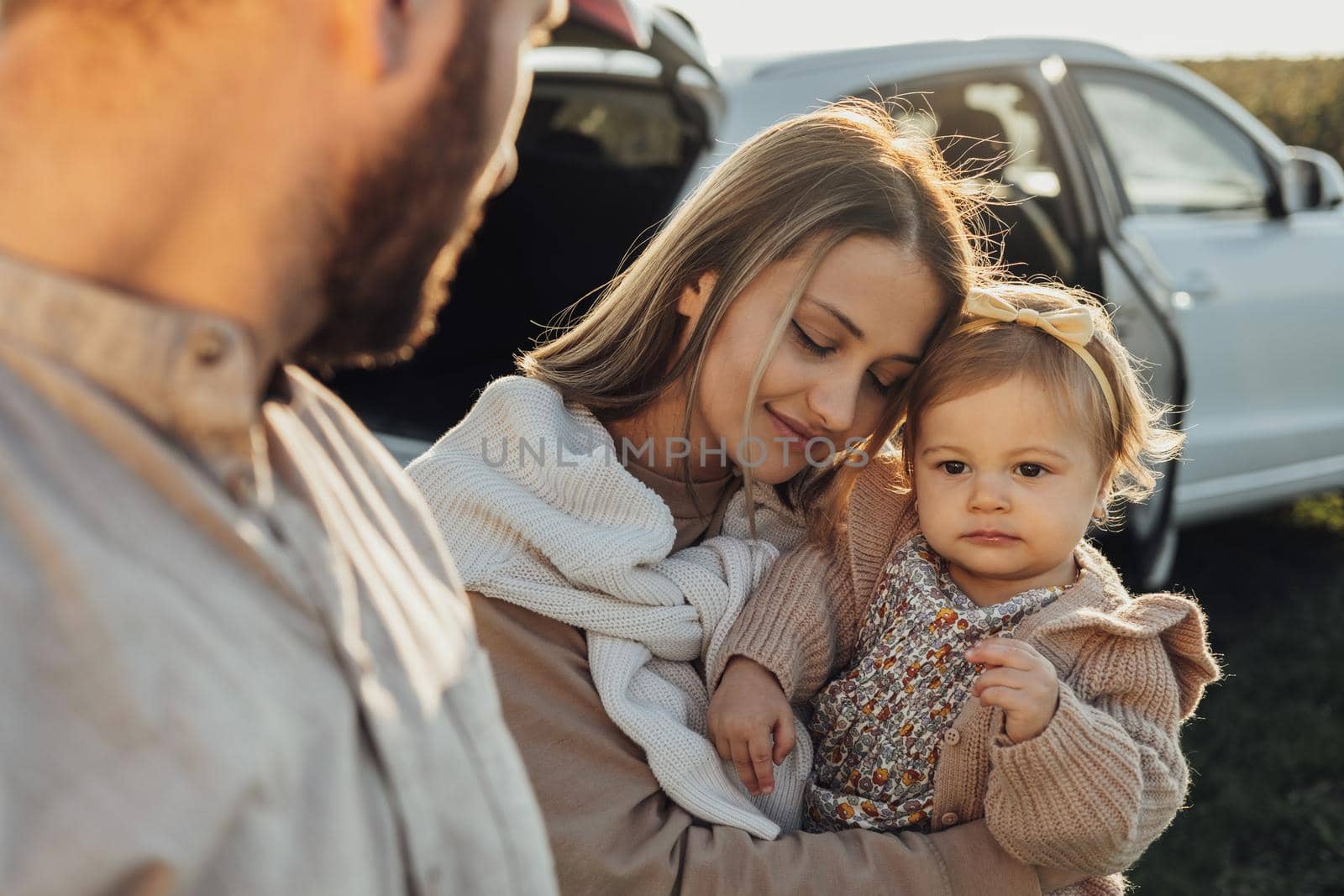 Young Caucasian Family Enjoying Road Trip, Mother and Father with Little Daughter Outdoors with SUV Car on the Background by Romvy