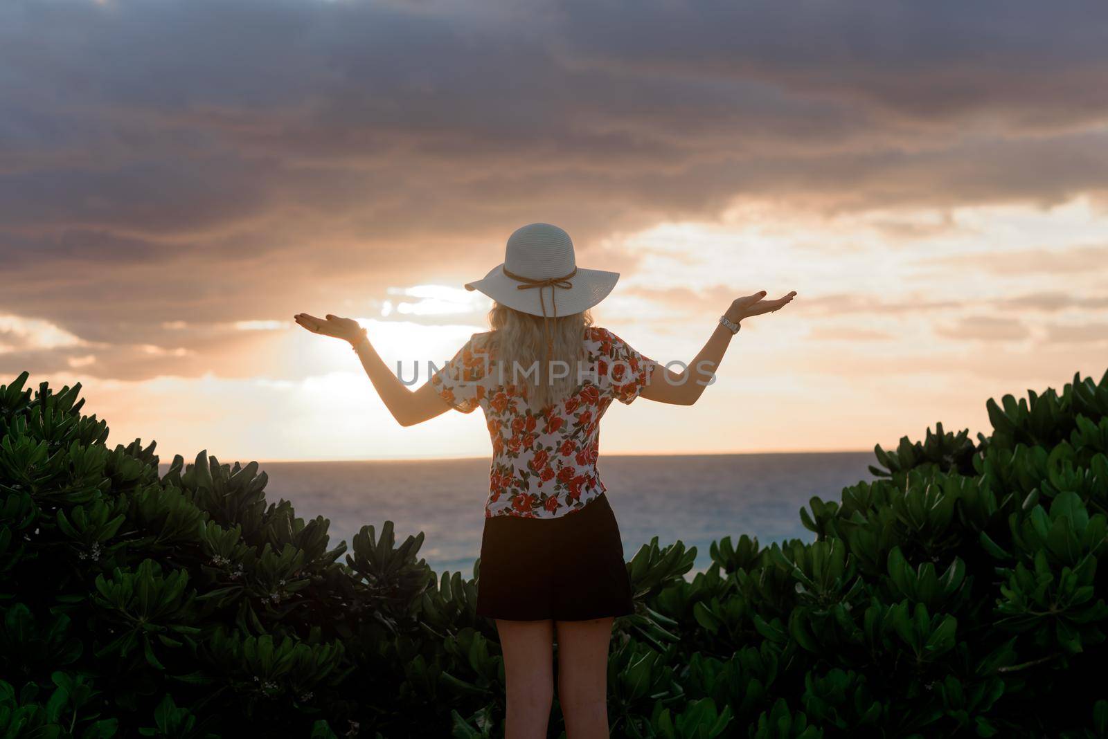 Slender blonde woman admires the sunrise at sea.