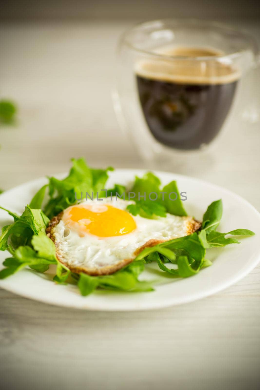 one fried egg with arugula and lettuce in a plate on a wooden table