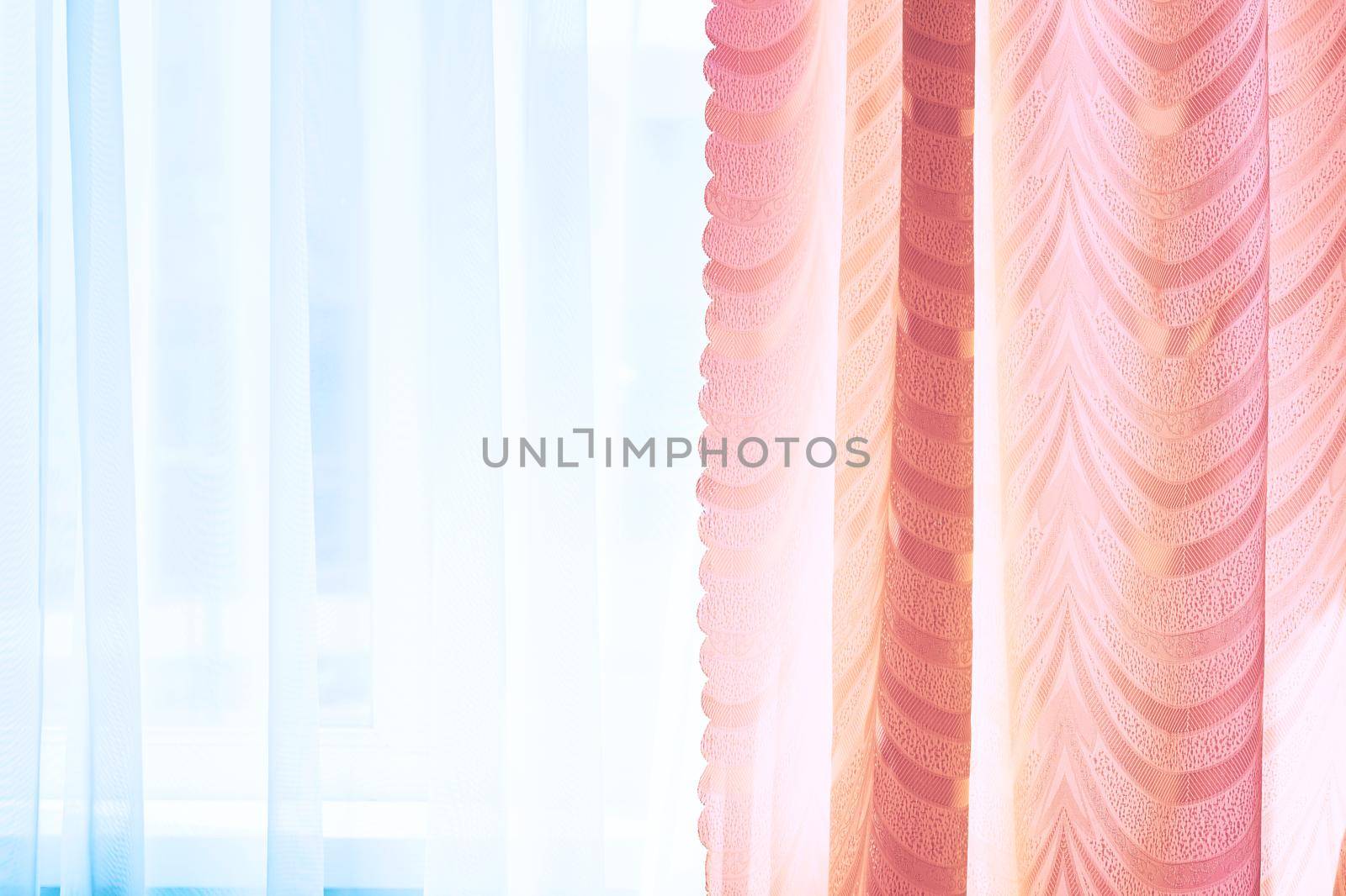 a piece of material suspended at the top to form a covering or screen, typically one of a pair at a window. Golden curtains and tulle on the window in the warm midday sun