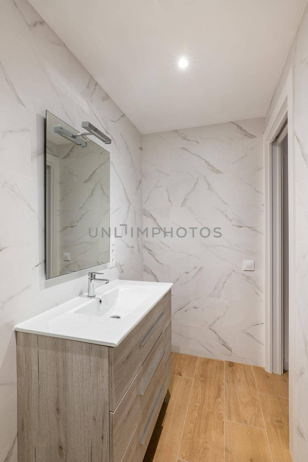 Bathroom with white tiles, mirror, ceramic sink under a wardrobe in a modern house or office