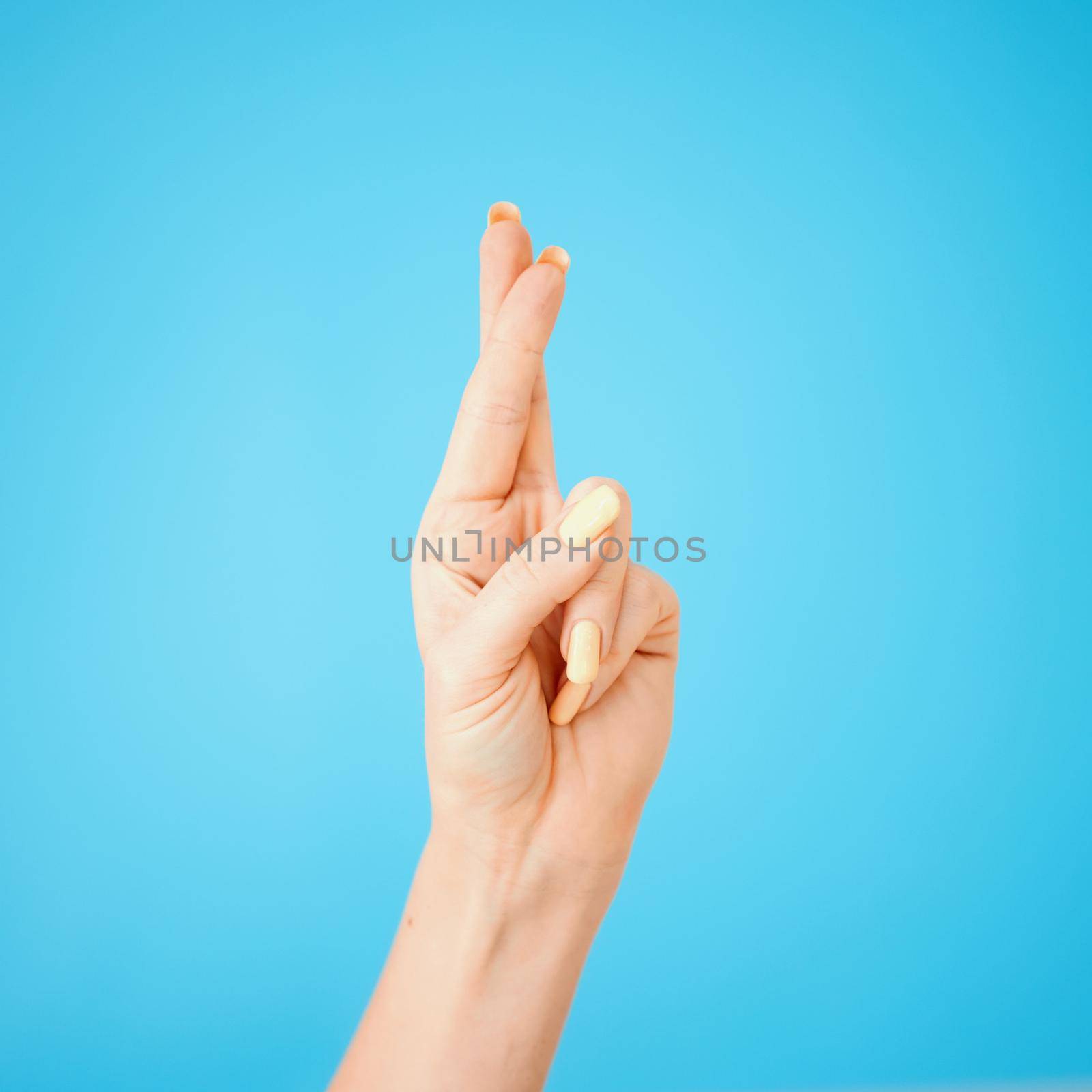 I hope I get it. Studio shot of an unrecognisable woman crossing her fingers against a blue background. by YuriArcurs