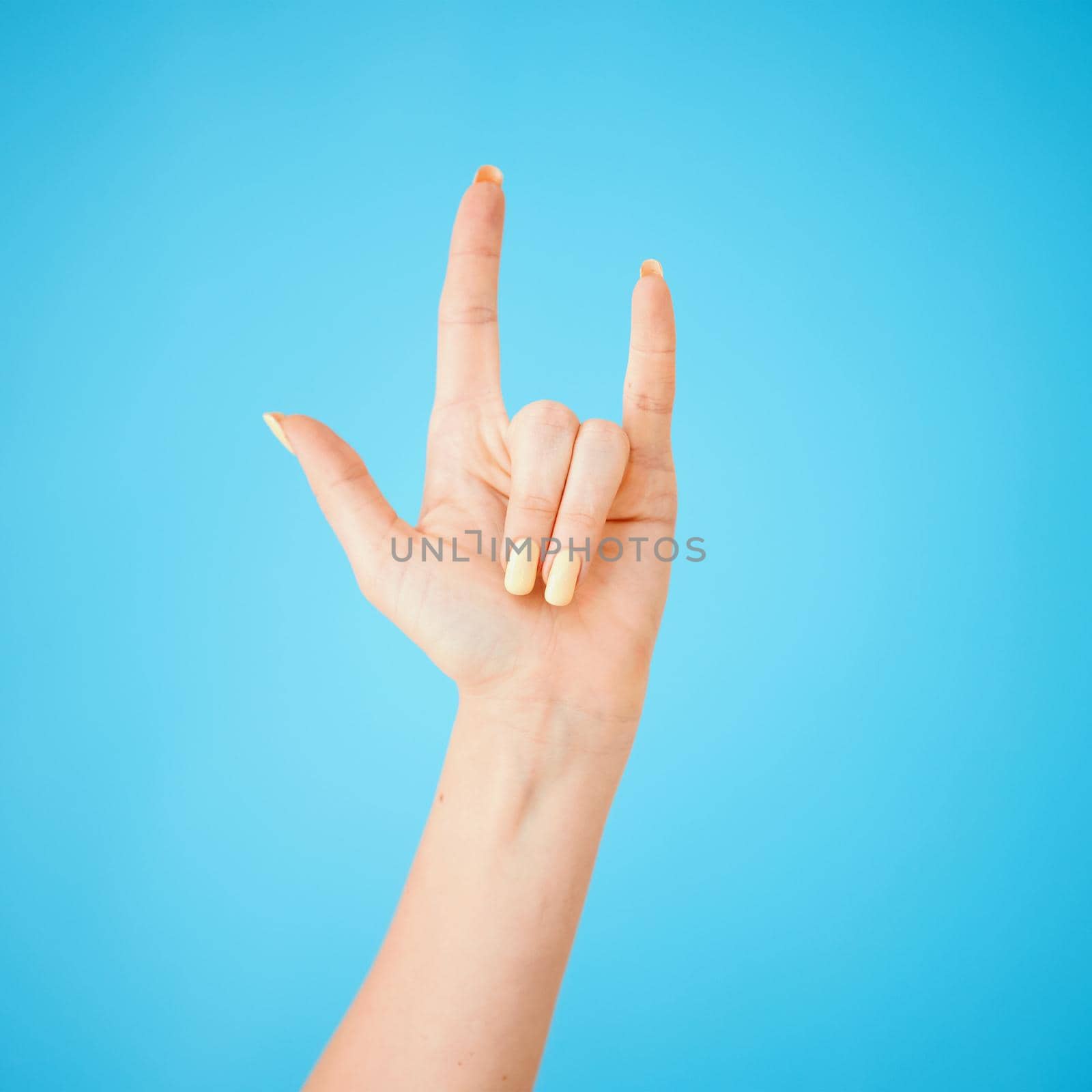 Party on my people. Studio shot of an unrecognisable woman making a horn sign against a blue background. by YuriArcurs
