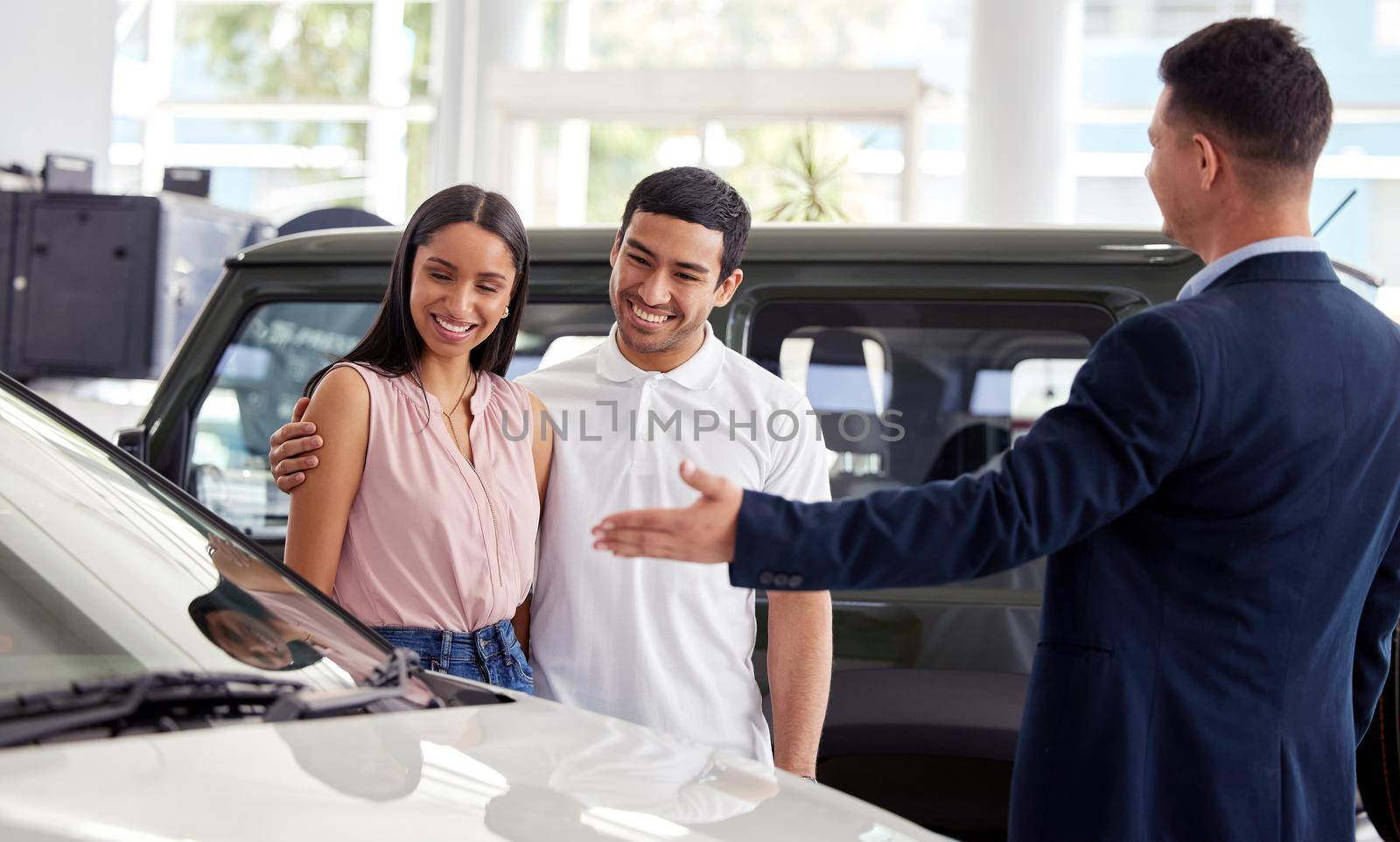 This beauty just came in. a car salesman assisting a young couple on the showroom floor. by YuriArcurs