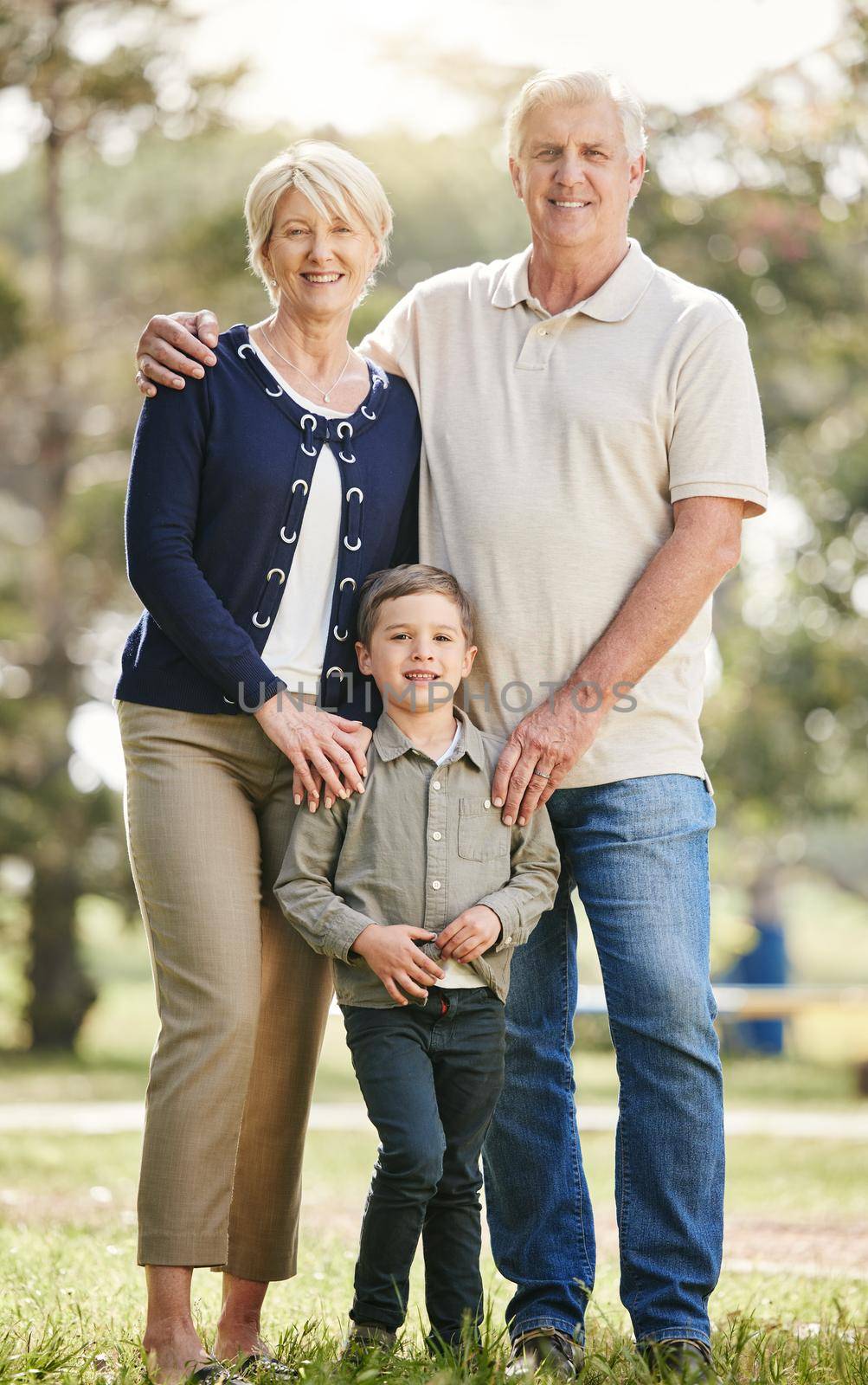 Portrait of loving caucasian grandparents enjoying time with grandson in nature. Smiling little boy bonding with grandmother and grandfather. Happy seniors and child standing together outdoors.