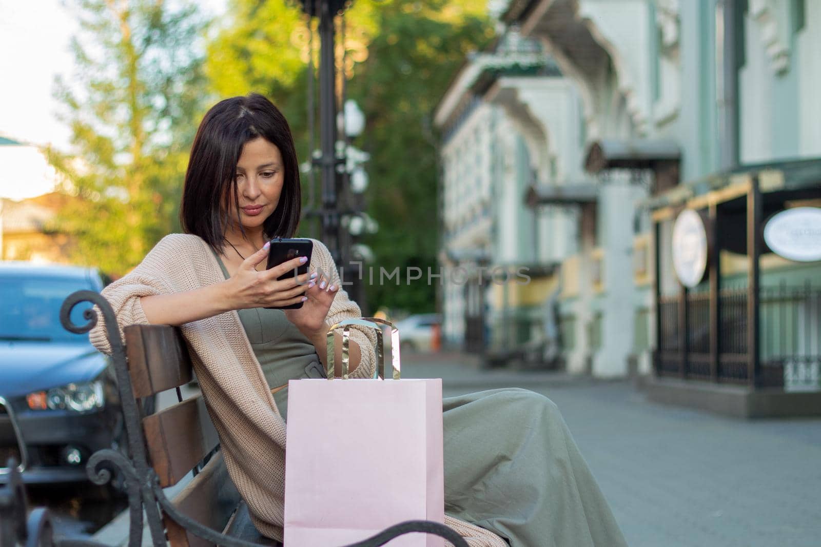 Young beautiful shopper woman smiling happy going to the shops sales holding shopping bags ourtdoors, smiling happy using smartphone
