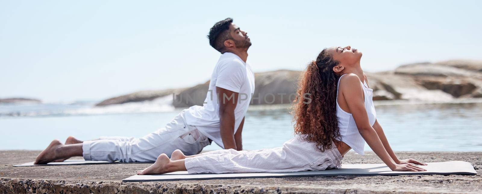 Full length shot of a young couple practicing yoga at the beach.