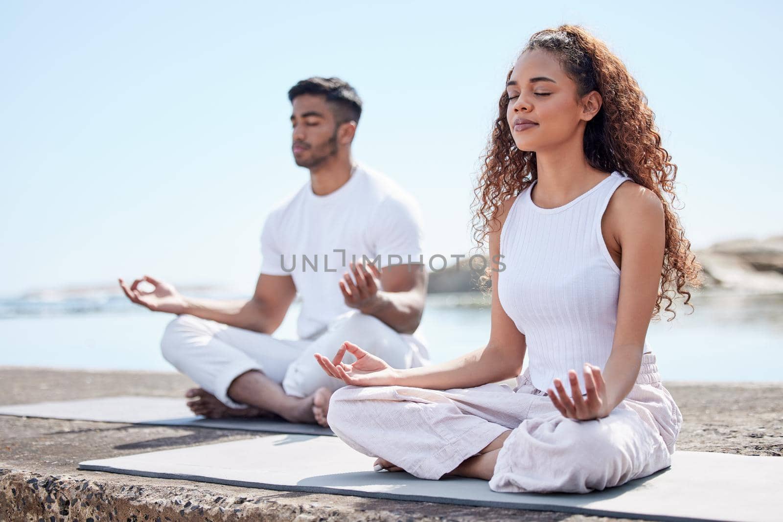 Just a couple of yoga enthusiasts. Full length shot of a young couple practicing yoga at the beach. by YuriArcurs