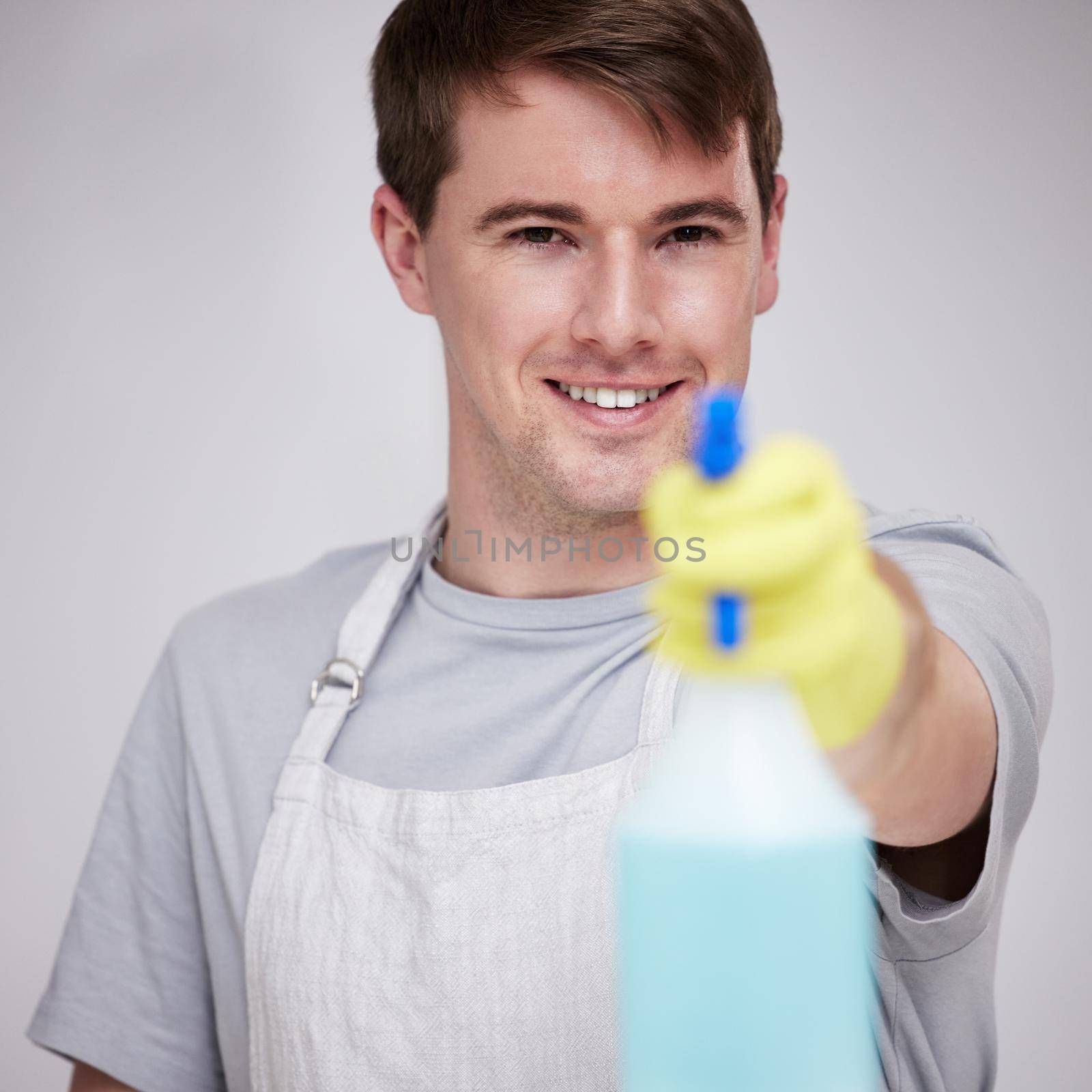 a young man holding a spray bottle against a grey background.