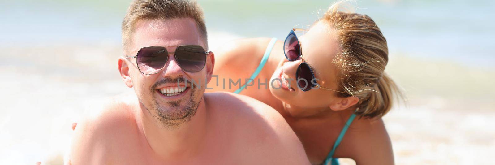 Portrait of cheerful couple resting together on beach laying on coastline and posing. Middle aged man and pretty woman in sunglasses. Beach, summer concept