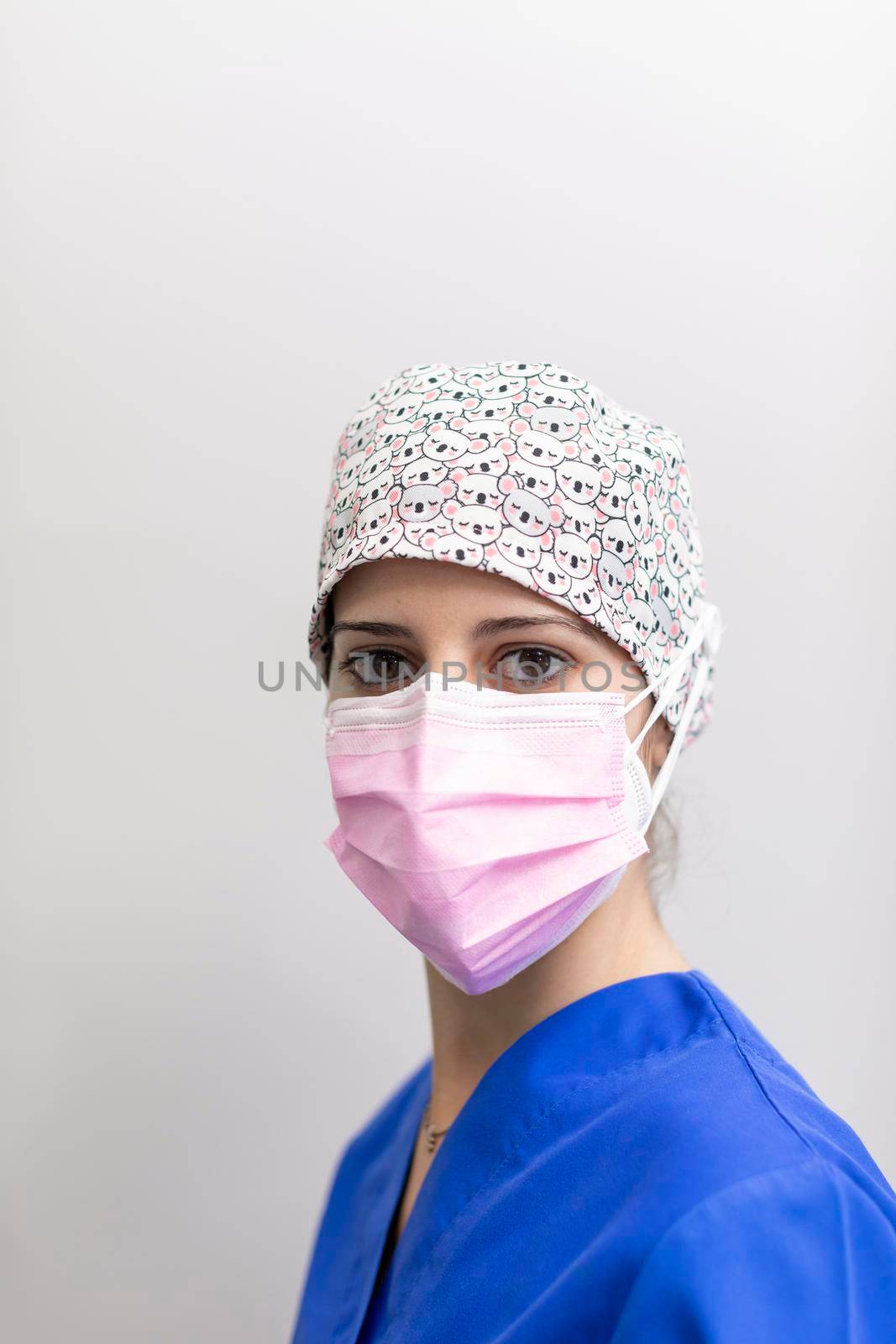 Portrait of a white dentist woman posing for the camera, wearing mask and medical hat and uniform after a day of work at the dental clinic hall