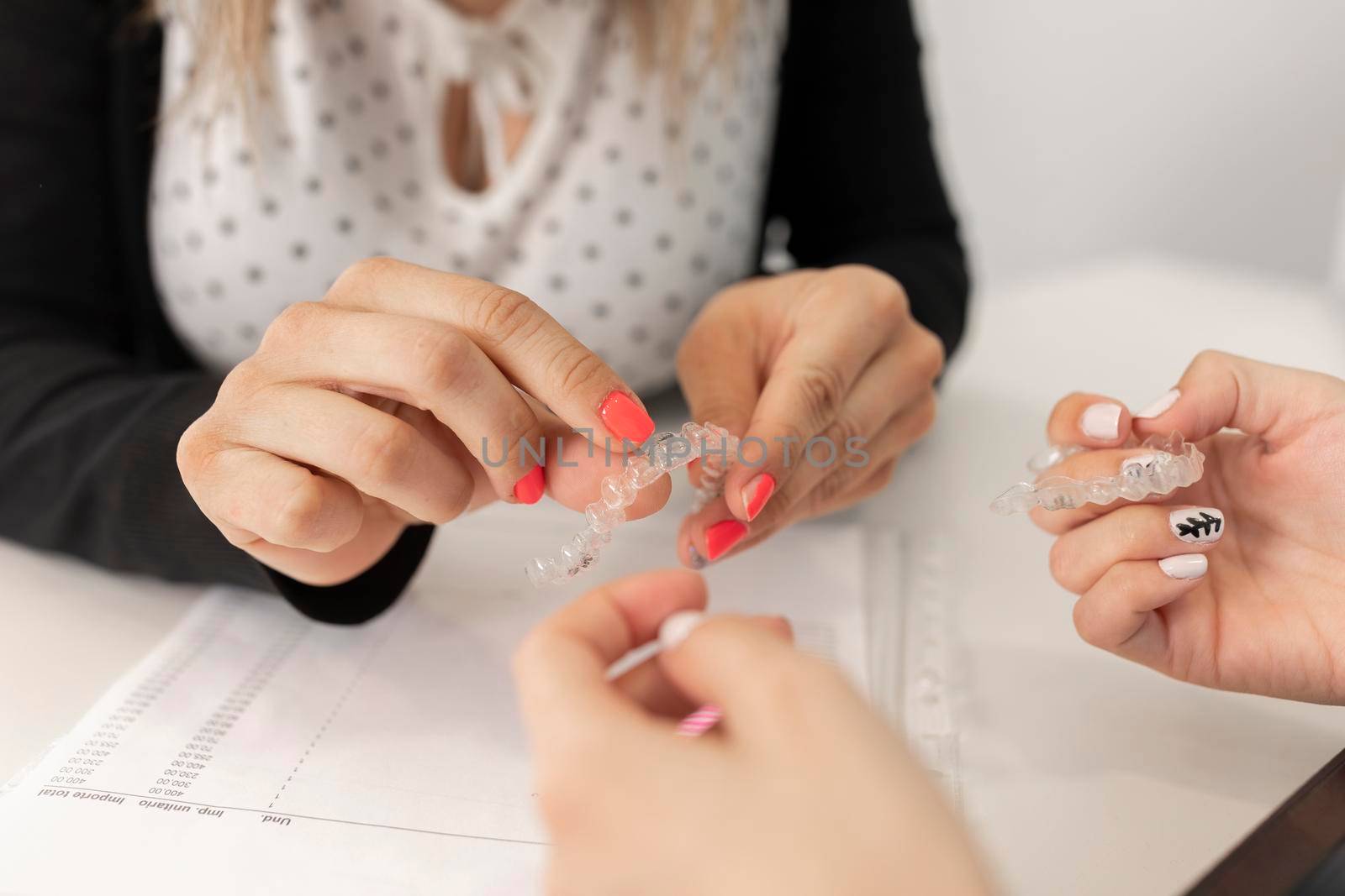 Hands of a manager woman showing to one of her employees some aspects of invisible orthodontics while holding it at the dental clinic