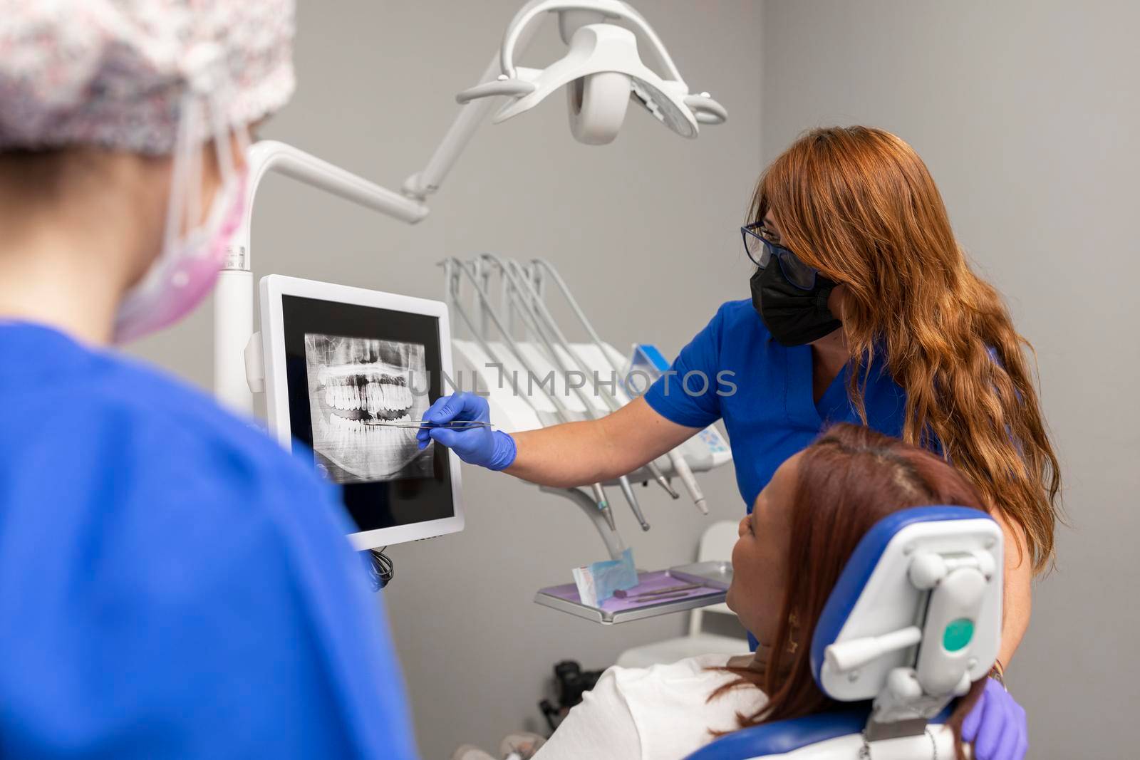 A dentist woman explains to her client the treatment that she is going to recieve while pointing at the radiography at the dental clinic